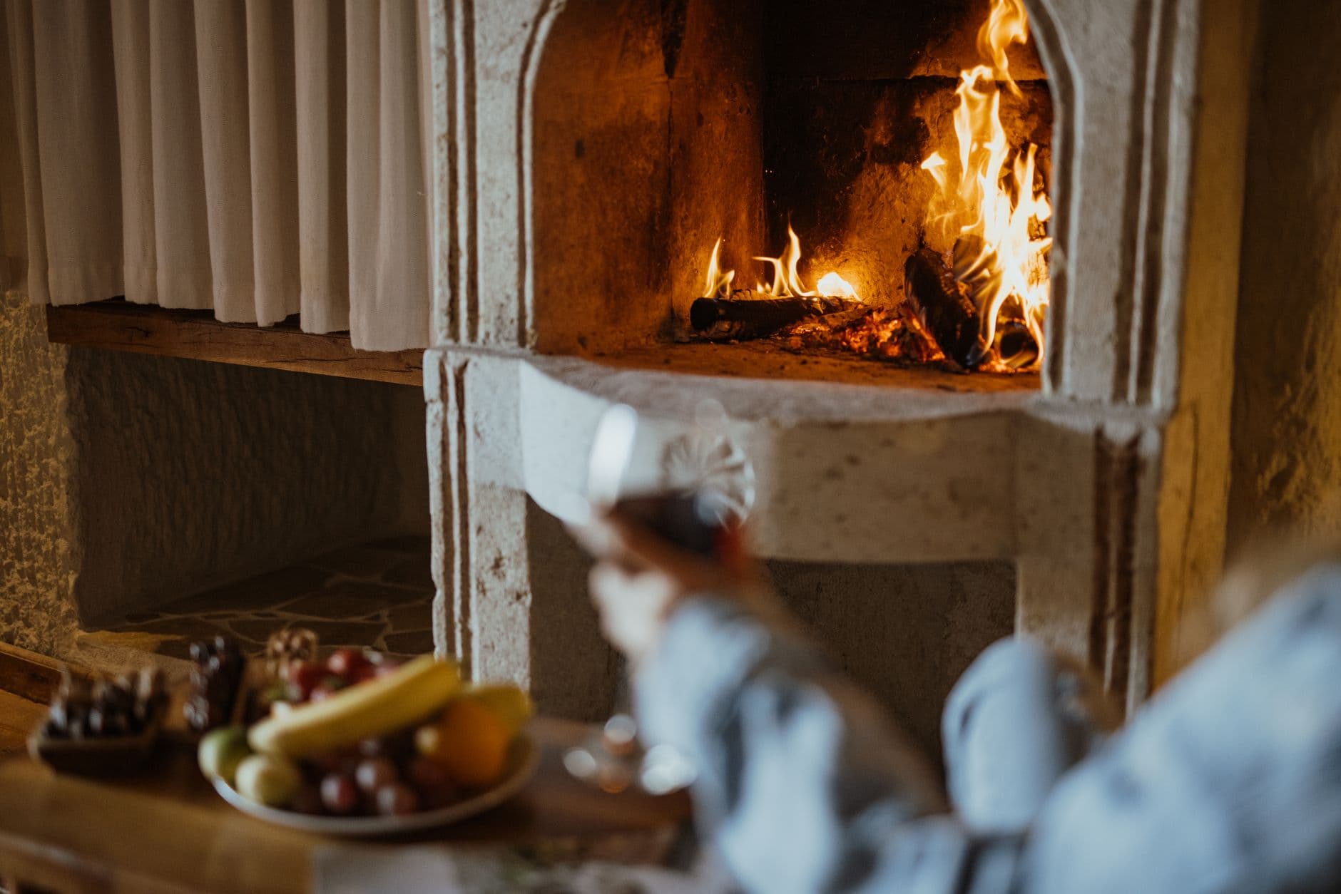 Warm stone fireplace with fruit and wine, creating a cozy, rustic atmosphere indoors.
